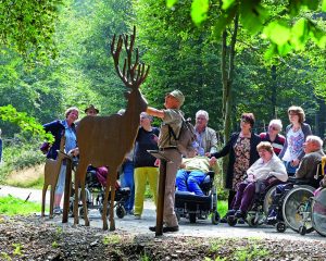 Waldführer Joseph Noel begleitet eine Gruppe von Rollstuhlfahrern mit ihren Angehörigen und Betreuern auf dem barrierefreien Naturerkundungspfad "Wilder Weg" in der Eifel.